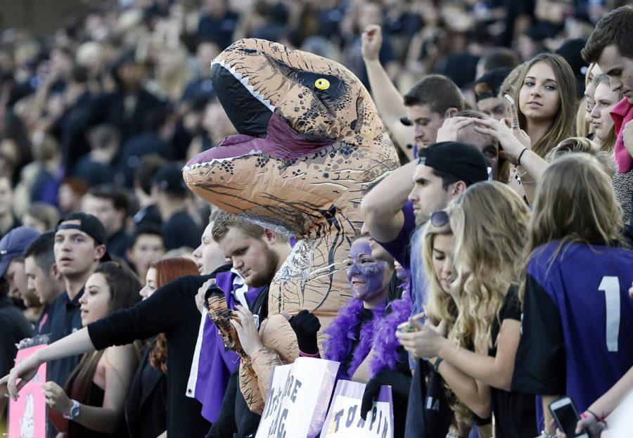 A person dressed in a dinosaur costume stands on the front row with other fans before the start of an NCAA college football game between West Virginia and TCU Thursday, Oct. 29, 2015, in Fort Worth, Texas. (AP Photo/Tony Gutierrez)