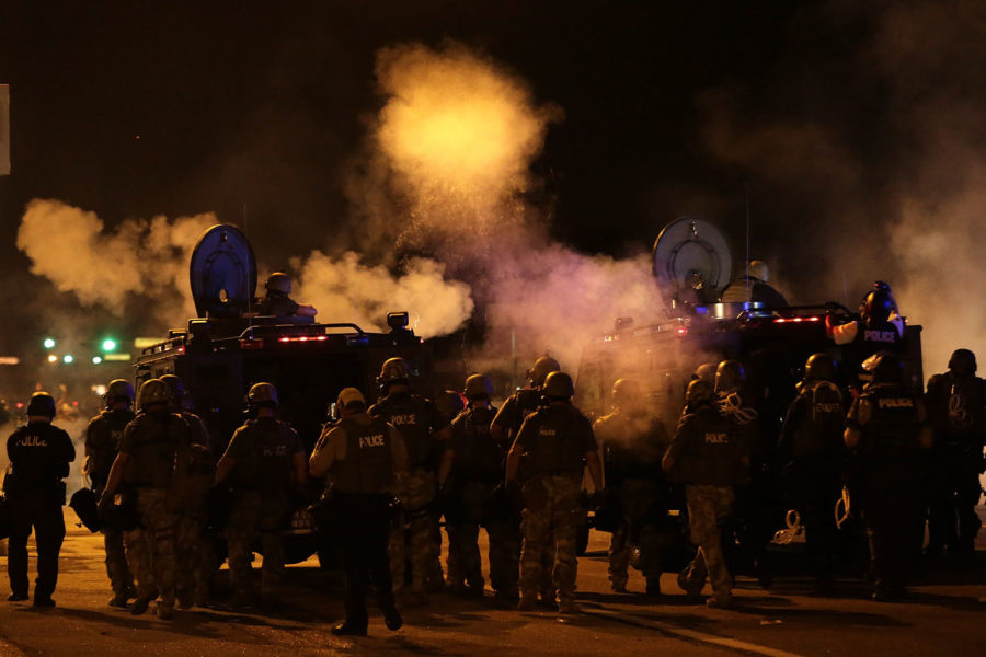 Police wait to advance after tear gas was used to dispersed a crowd Sunday, Aug. 17, 2014, as they staged a protest for Michael Brown, who was killed by police, last Saturday in Ferguson, Mo. Brown's shooting in the middle of a street, following a suspected robbery of a box of cigars from a nearby market, has sparked a week of protests, riots and looting in the St. Louis suburb. (AP Photo/Charlie Riedel)