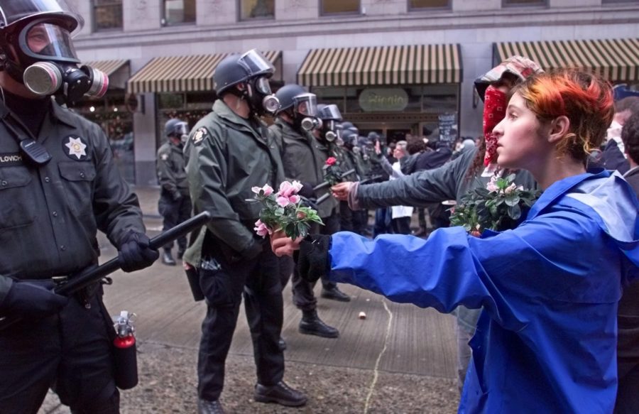 A demonstrator hands over flowers to Seattle police officers during demonstrations  against the World Trade Organization in downtown Seattle Tuesday, Nov. 30, 1999. Demonstrators temporarily succeeded in delaying the opening session of the WTO. (AP Photo/Itsu Inouye)