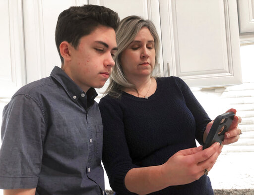 Grant Thompson and his mother, Michele, look at an iPhone in the familys kitchen in Tucson, Ariz., on Thursday, Jan. 31, 2019. The 14-year-old stumbled upon a bug in the iPhones FaceTime group-chatting feature on Jan. 19 while calling his friends to play a video game. With the bug, a FaceTime group-chat user calling another iPhone, iPad or Mac computer could hear audio, even if the receiver did not accept the call. (AP Photo/Brian Skoloff)