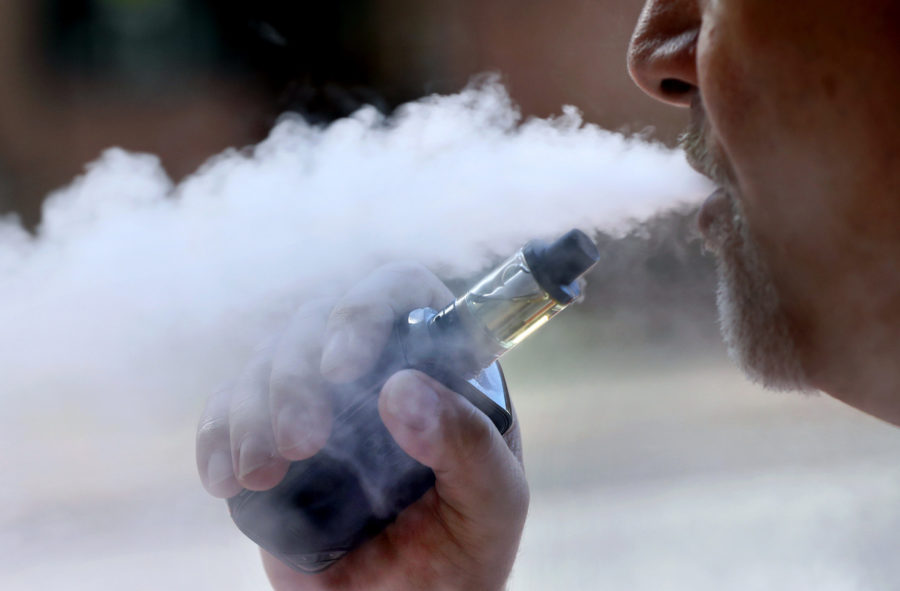 File - In this Aug. 28, 2019, file photo, a man exhales while smoking an e-cigarette in Portland, Maine. The U.S. government has refined how it is measuring an outbreak of breathing illnesses in people who vape, now counting only cases that are most closely linked to electronic cigarette use. Health officials on Thursday, Sept. 12, 2019 said 380 confirmed cases and probable cases have been reported in 36 states and one U.S. territory.  (AP Photo/Robert F. Bukaty, File)