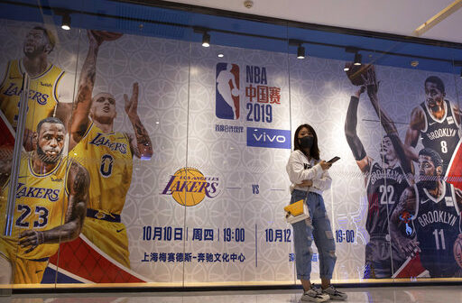 A woman wearing a mask stands near promotion boards for a NBA preseason game between Brooklyn Nets and Los Angeles Lakers in Beijing. (AP Photo/Ng Han Guan)