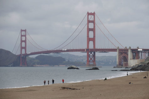 A small group of people walk in front of the Golden Gate Bridge at Baker Beach in San Francisco, Saturday, March 28, 2020, amid the COVID-19 coronavirus outbreak. (AP Photo/Jeff Chiu)