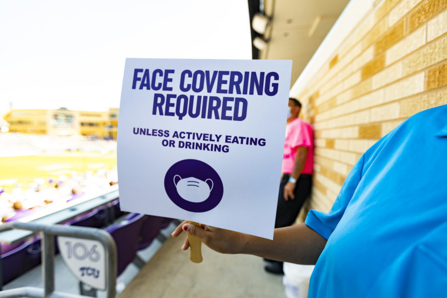 A stadium employee holds a sign reminding fans to wear a mask.