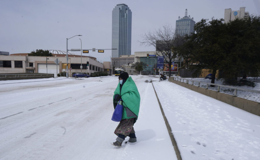FILE - In this Feb. 16, 2021, file photo, a woman wrapped in a blanket crosses the street near downtown Dallas. As temperatures plunged and snow and ice whipped the state, much of Texas power grid collapsed, followed by its water systems. Tens of millions huddled in frigid homes that slowly grew colder or fled for safety. (AP Photo/LM Otero, File)