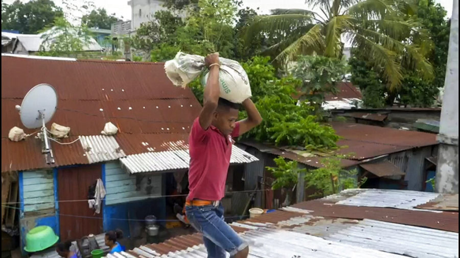 In this image made from video, a man carries a sandbag to secure his tin roof Friday Feb. 4, 2022 in Toamasina as he prepares for Tropical Cyclone Batsirai to make landfall in central Madagascar. The Global Disaster Alert and Coordination System says Batsirai has been upgraded and classified as Category 4.(AP Photo)