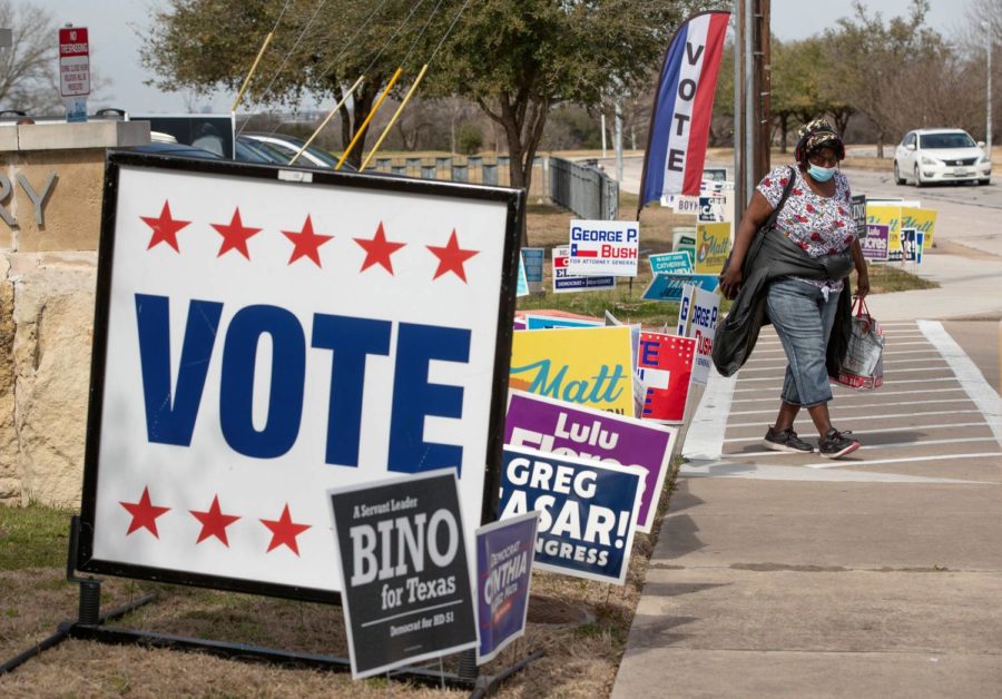 Debra Kerr walks past campaign signs at a polling place at Dan Ruiz Branch Library on Texas Primary Election Day on Tuesday March 1, 2022, in Austin, Texas. Voters in Texas are ushering in the midterm campaign season with primaries Tuesday. (Jay Janner/Austin American-Statesman via AP)