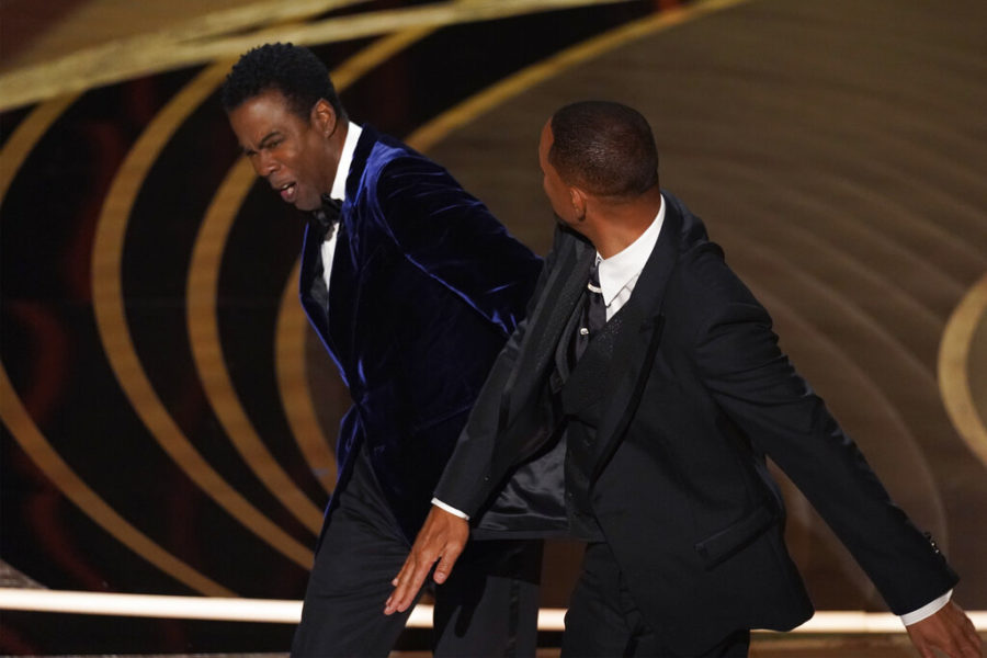 FILE - Will Smith, right, hits presenter Chris Rock on stage while presenting the award for best documentary feature at the Oscars on Sunday, March 27, 2022, at the Dolby Theatre in Los Angeles. The incident on Sunday has sparked debate about the appropriate ways for Black men to publicly defend Black women against humiliation and abuse. (AP Photo/Chris Pizzello, File)