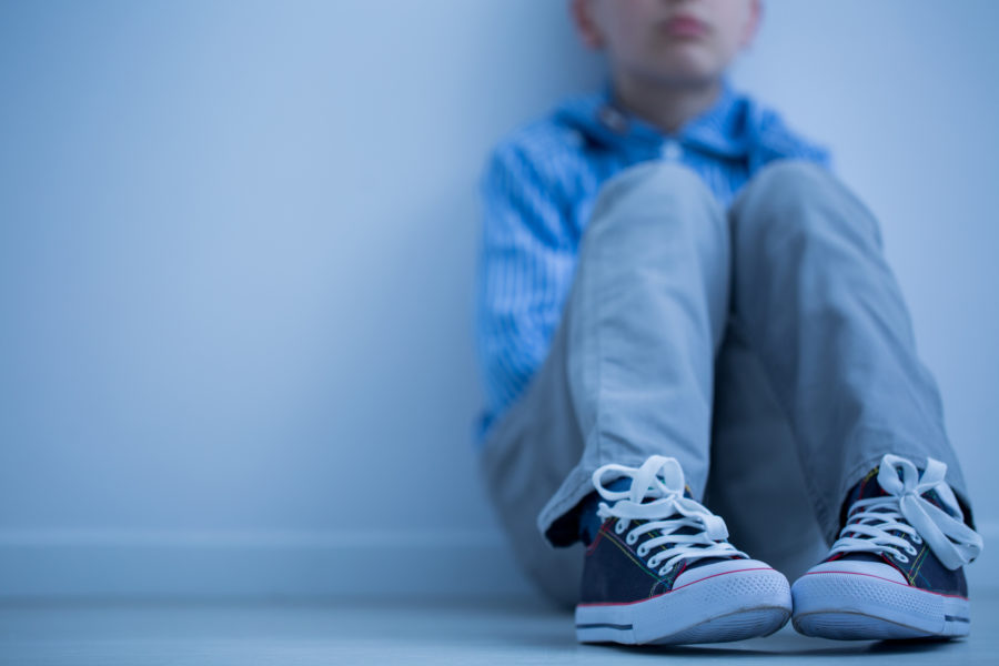 Sad boy in sneakers with aspergers syndrome sits alone in his room. (iStock.com/KatarzynaBialasiewicz)