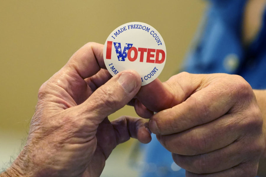 Gary Wilson, right, a poll worker in a Rankin County precinct, hands an I Voted sticker to a person who filled out a ballot Tuesday, Nov. 8, 2022. (AP Photo/Rogelio V. Solis)