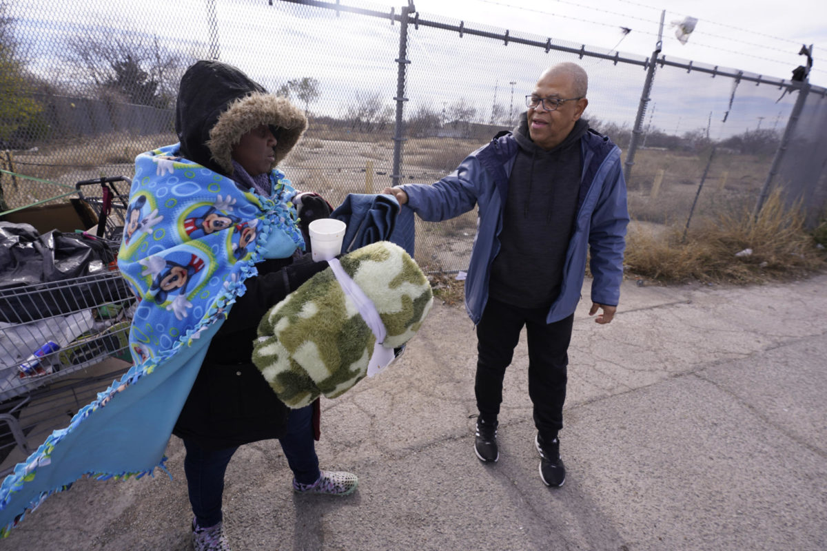 Bruce Butler, right, hands a blanket to Mika, who is homeless, to help her with the cold weather in Fort Worth, Texas, Friday, Dec. 23, 2022. (AP Photo/LM Otero)