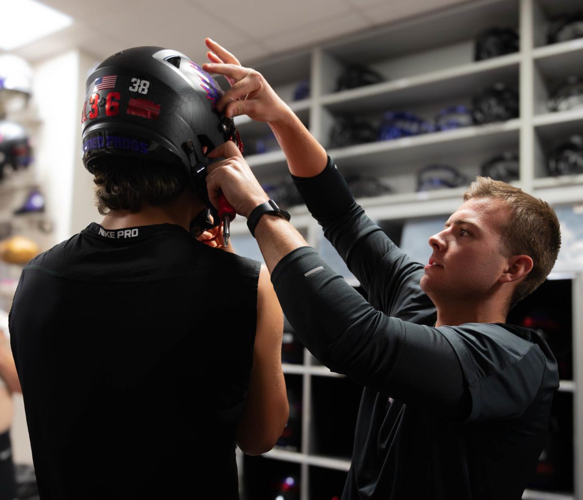 TCU equipment manager Brayson Melton fits a helmet on wide receiver Joe Laterza prior to TCU's home game against Baylor in 2023.