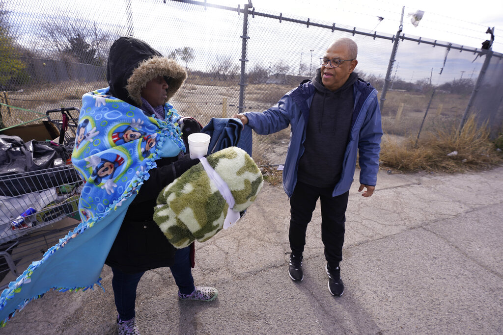 Bruce Butler, right, hands a blanket to Mika, who is homeless, to help her with the cold weather in Fort Worth, Texas, Friday, Dec. 23, 2022. (AP Photo/LM Otero)